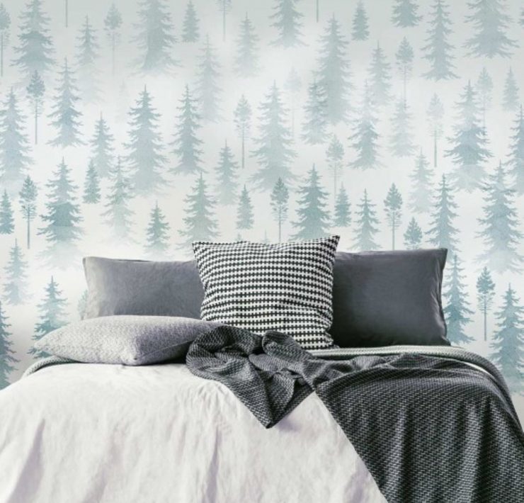 A wall mural made of many layers of tree stencils behind a bed.