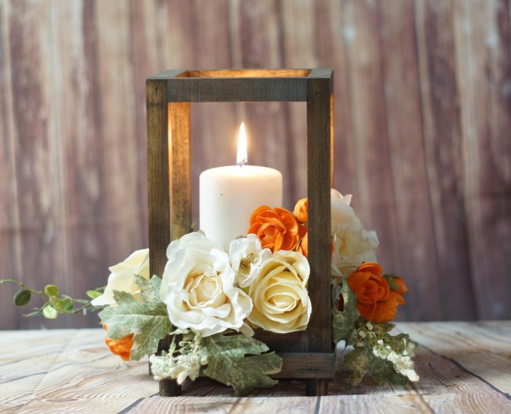 Wooden candle holder surrounding a lit candle with bright orange flowers around the edges