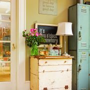 A cream-colored vintage desk with a lamp, bouquet of flowers and teal vintage lockers next to it demonstrates how to decorate with what you already have.