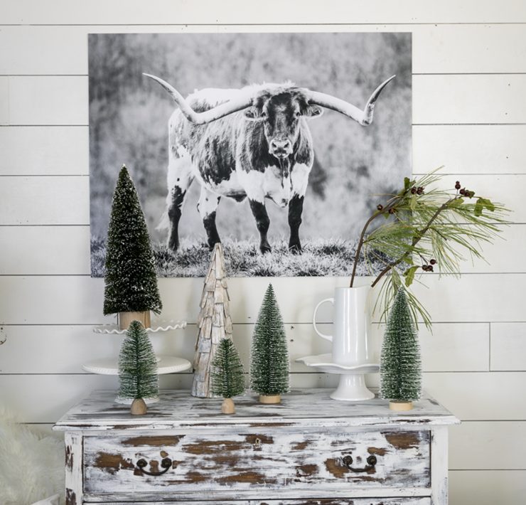 Plain mini pine trees on top of a rustic, faded white dresser.