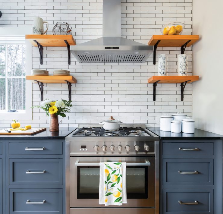 The kitchen has bluejay blue counters covered in black countertops. The white backsplash is paired with open farmhouse wood shelves