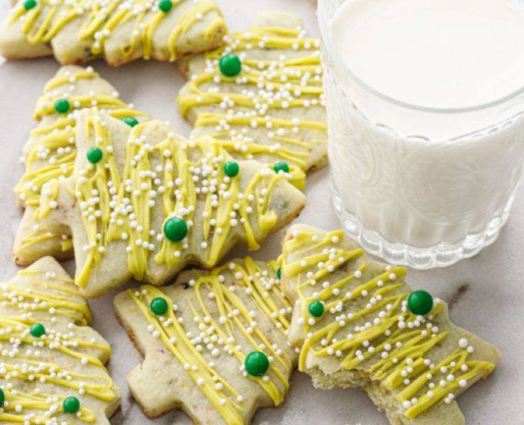 A plate with pistachio sugar cookies cutout into Christmas trees and a glass of milk