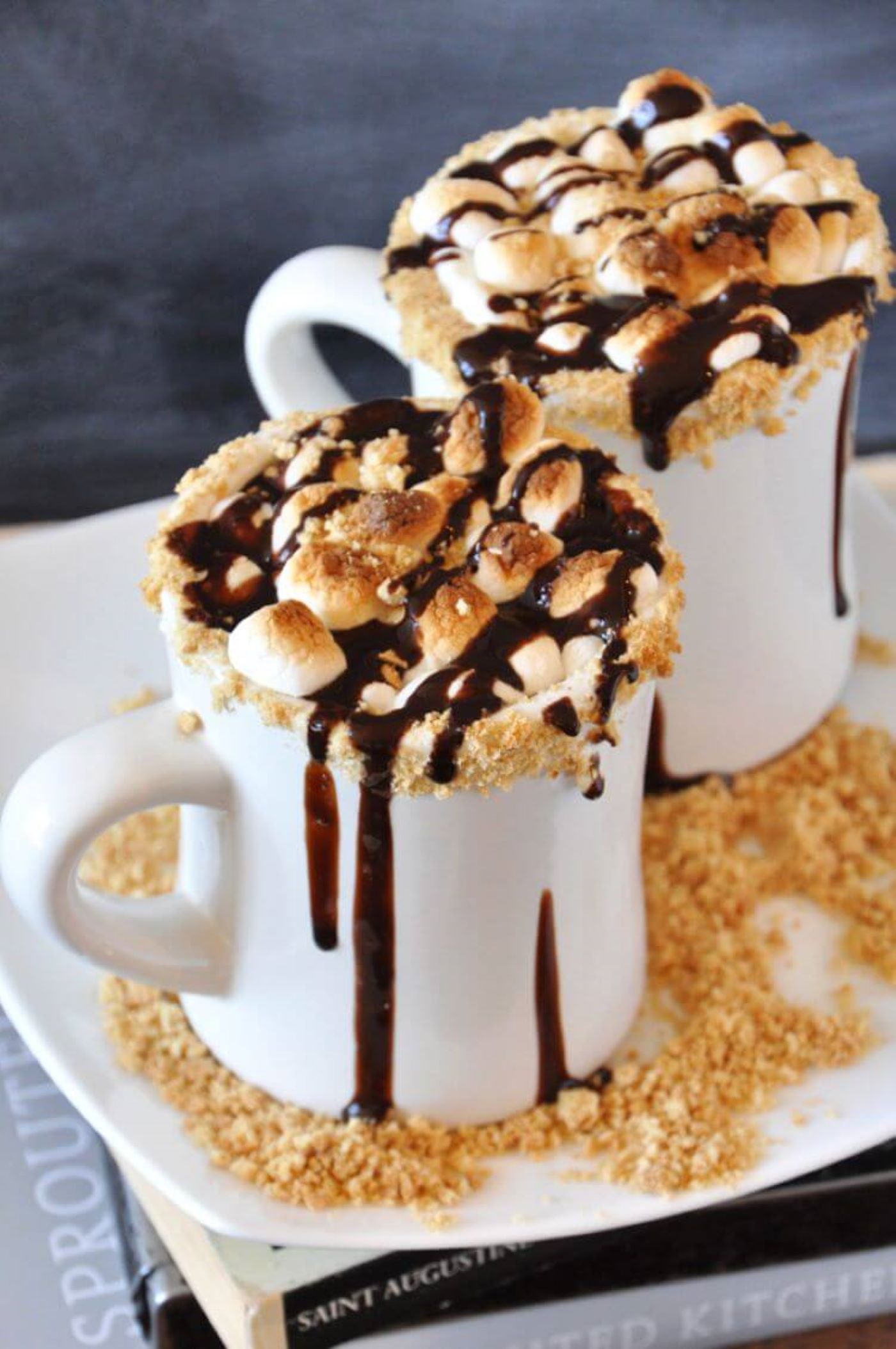 Gooey marshmallows clump together in a cup of hot chocolate brimming with chocolate syrup and gram cracker shavings.