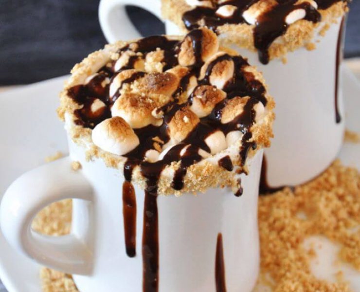 Gooey marshmallows clump together in a cup of hot chocolate brimming with chocolate syrup and gram cracker shavings.