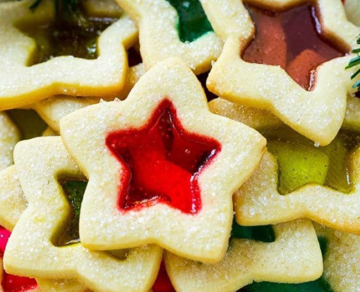 A plate of stained glass sugar cookies cut into stars with rainbow windows under a Christmas tree