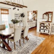 A dining room with a wood floor and a vintage style rug under a table and set of chairs. Above the table is a chandelier made with lights strung through a flea market painter’s ladder.