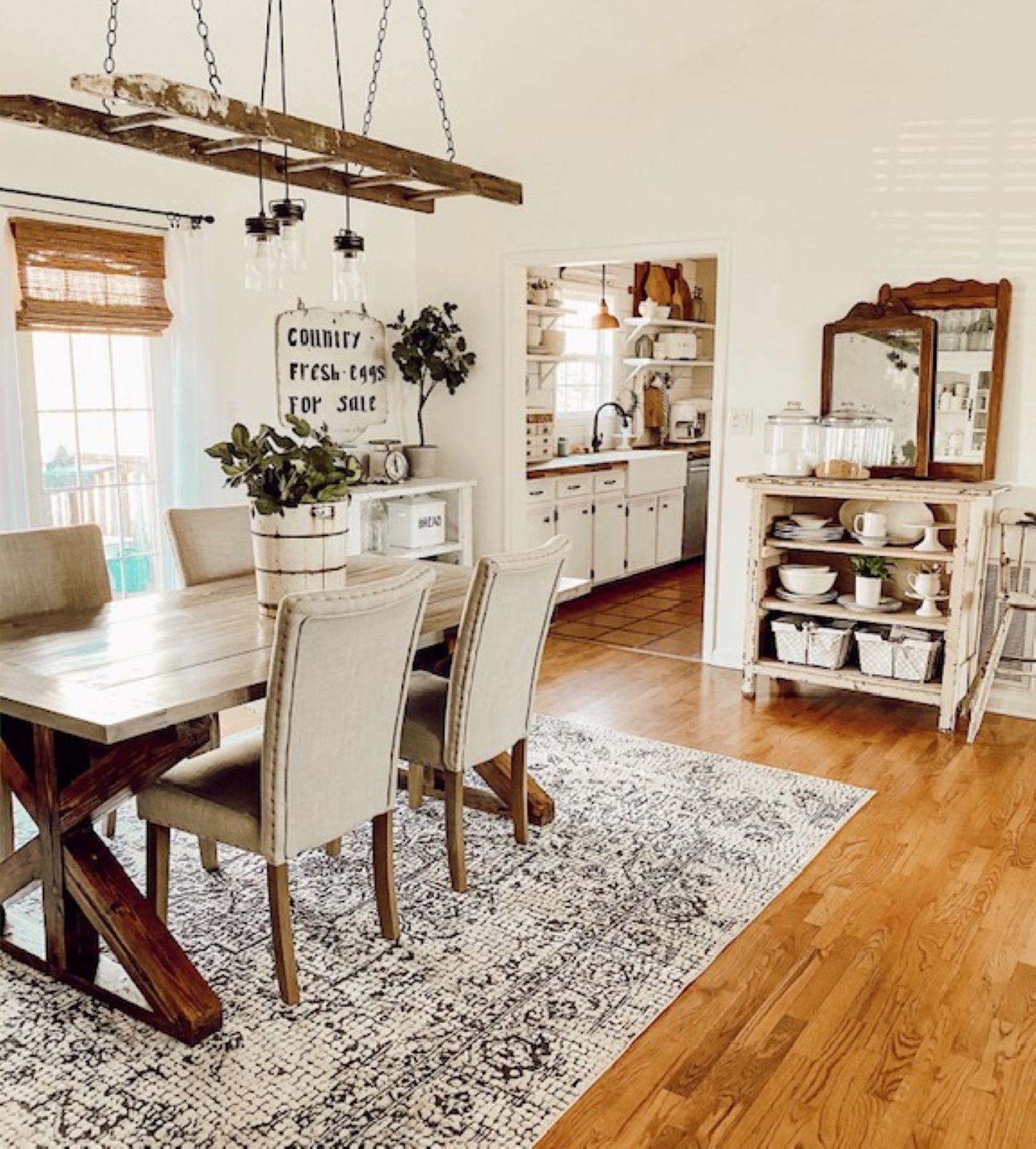 A dining room with a wood floor and a vintage style rug under a table and set of chairs. Above the table is a chandelier made with lights strung through a flea market painter’s ladder.