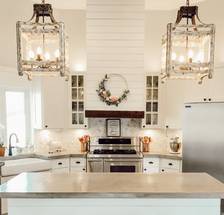 A white farmhouse kitchen with poured concrete countertops and white shiplap beside two large pendant lights