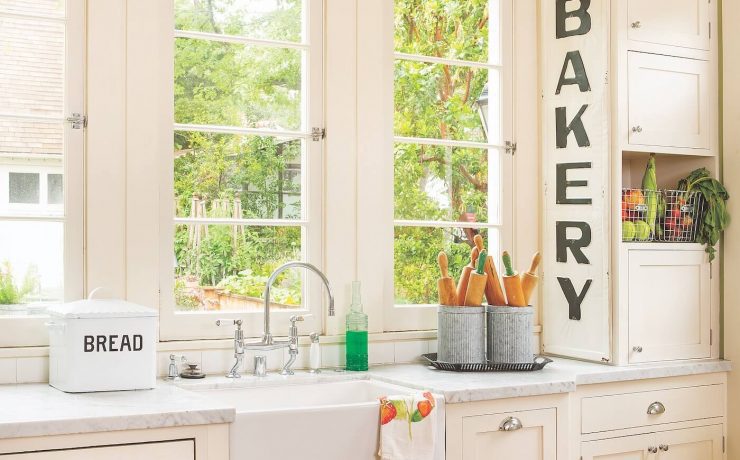A kitchen painted in sage green on the walls and white cabinets and clean countertops. a large sign says Bakery near the clear windows.