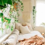 A boho bedroom with cream throw pillows and hanging plants.