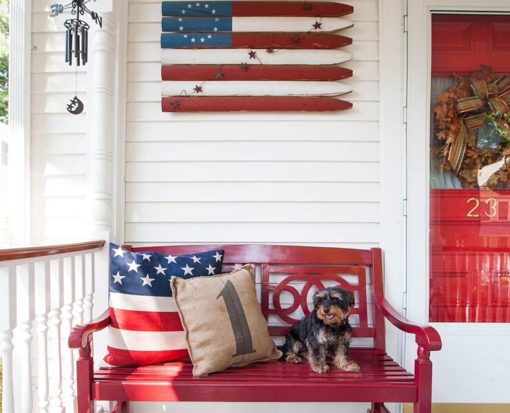 4th of July porch set up with red front door and bench and American flag wooden sign.