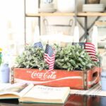 Antique red Coca-Cola crate filled with mini flags and greenery.