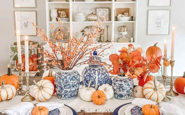 A blue and white toile style tablescape is filled with pops of orange in the pumpkins and fall foilage