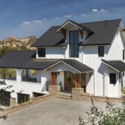 The remodeled exterior of the Farmhouse is warm and welcoming with white board and batten walls, a standing seam black metal roof, wooden ornamental trim including oversized exterior corbels and pillars and a gorgeous stained Dutch door.